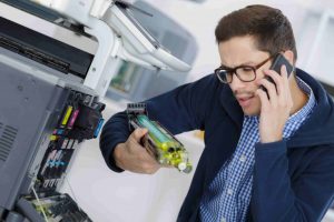 technicien au t&eacute;l&eacute;phone r&eacute;parant un photocopieur